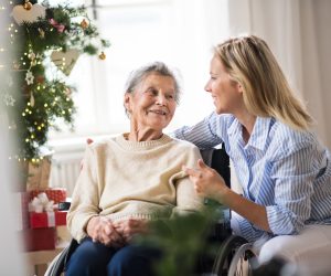 A senior woman in wheelchair with a health visitor at home at Christmas time, talking.